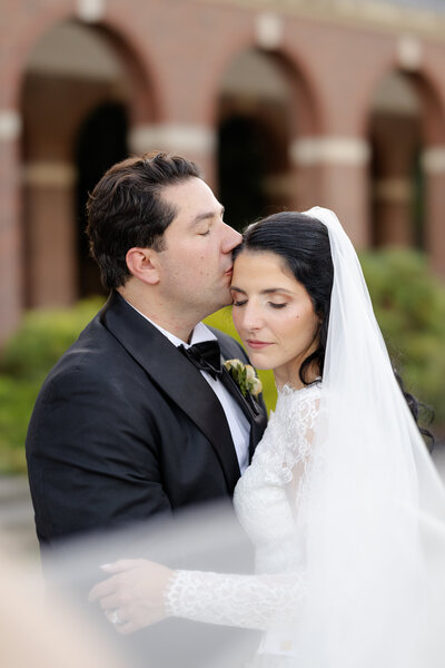Groom nuzzles his nose into the side of the bride's head while she looks over her shoulder
