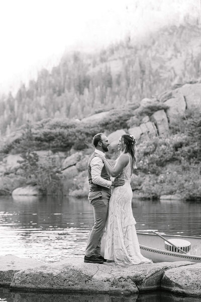 Newlyweds celebrating on a rock in a middle of pond in front of their guests cheering at sunset. at White Wolf resort in Alpine Palisades Tahoe  Black and white image