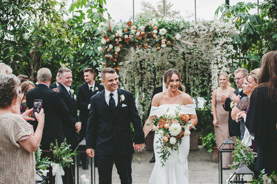 Alyssa Amez a custom wedding stationery and signage designer and business woman from Alyssa Amez Design as a bride on her wedding day at Planterra Conservatory in West Bloomfield, Michigan posing in her wedding dress and a flower bouquet in front of the wedding venue