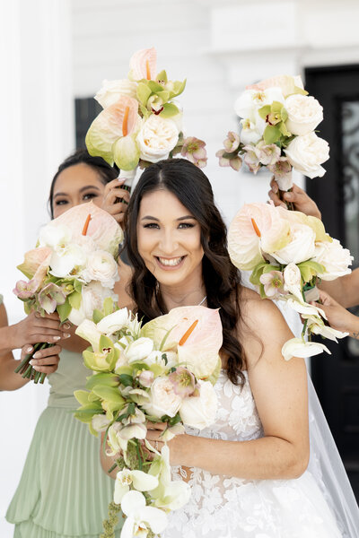 Bride smiling with bridesmaids holding tropical bouquets featuring anthuriums, orchids, and roses at Maison De Veaux wedding in Houston, Texas