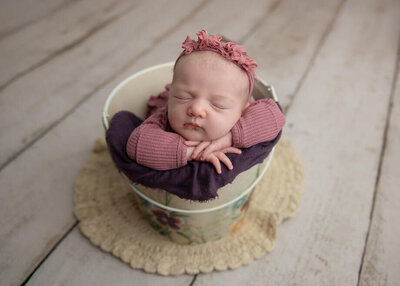 Baby girl on a dark neutral taupe backdrop with a matching knit wrap and a matching floral headband