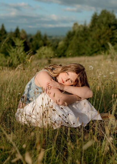 Girl sitting in a field with her hands on her arms staring in to the sun. 