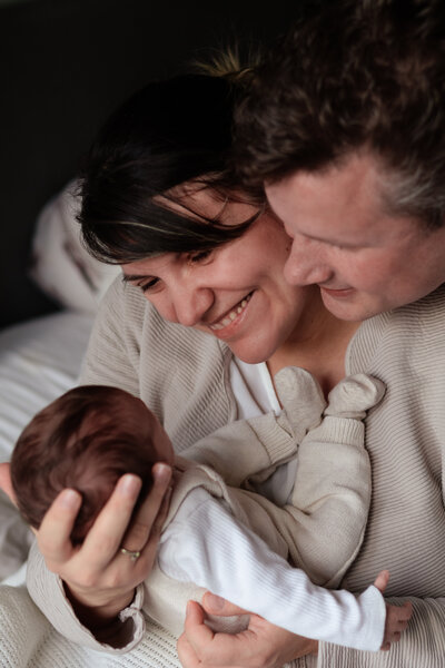 Een man en een vrouw houden een baby vast, stralend van vreugde en liefde in hun ogen.