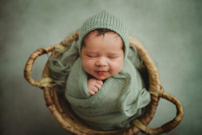 baby boy wrapped in a sage wrap snuggled into a boho basket