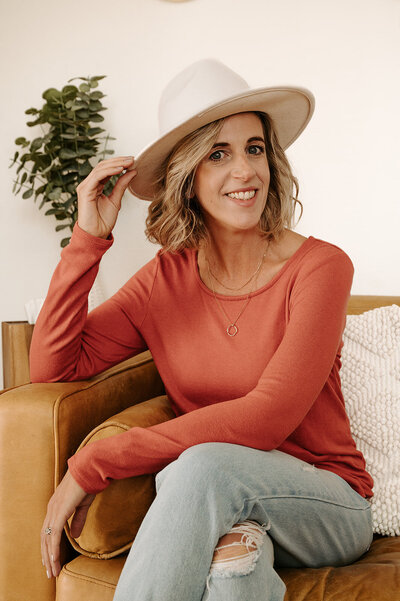 Claire holding a hat  sitting on a sofa, showit website designer