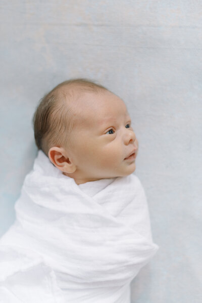 Portrait of a baby boy in a white swaddle on a blue watercolor mat