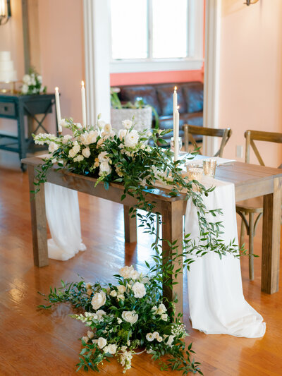 Elegant wedding reception centerpiece featuring lush floral arrangements with blush roses, greenery, and white hydrangeas, designed by Leigh Florist