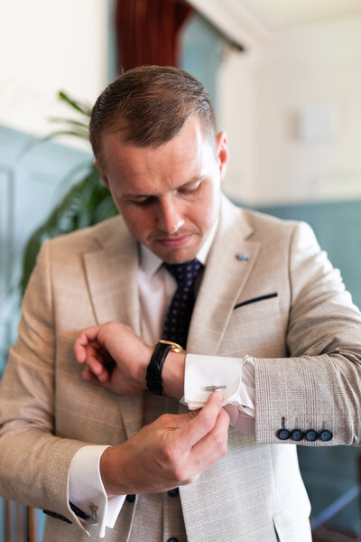 Groom looks down at his cufflinks while getting ready at The Beacon Tunbridge Wells