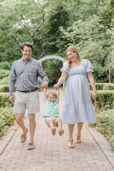 Parents swinging their toddler while walking down a garden path by Maternity Photographer Greenville SC.