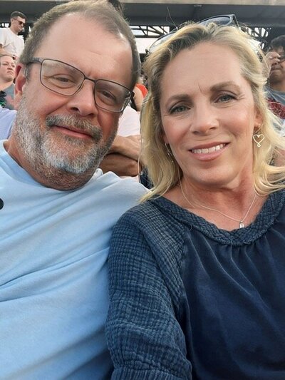 photo of husband and wife dressed in blue at a baseball game sitting in the stands.  both are smiling