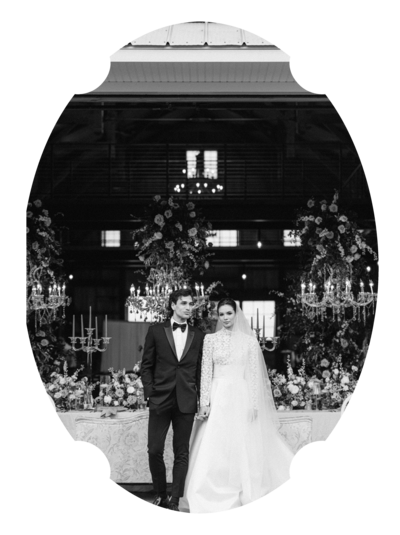 Black and white portrait of a bride and groom standing in front of a table decorated with large floral centerpieces