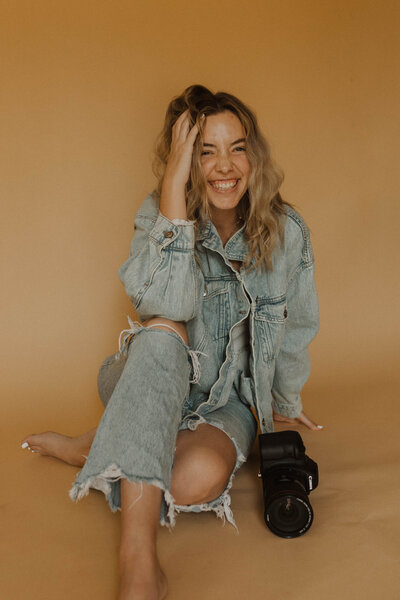 girl sitting on the floor smiling holding a camera