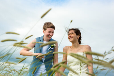 A couple holding hands and smiling while they walk through a field.