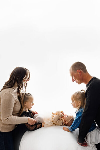 A family looks at their new baby in an all-white newborn studio.