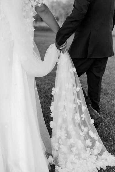 Black and white close-up photo of bride and groom holding hands on their wedding day.