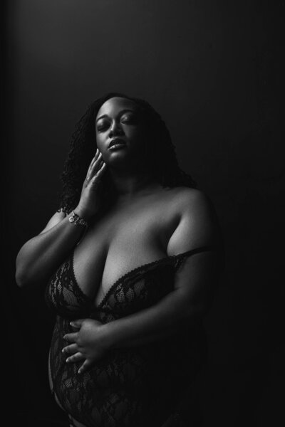 artistic photo of plus sixe woman standing with one hand lightly touching her face and the other embracing herself slightly