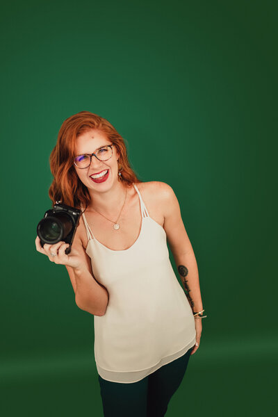 Meagan McGregor holding her camera and smiling on a green backdrop