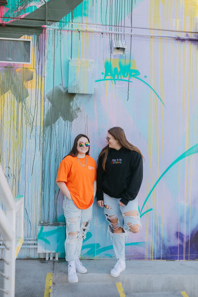 Two friends smiling in front of a painted mural