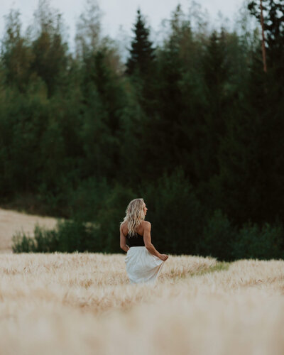 Naineen seisoo pellolla metsän laidalla ja pitelee hameenhelmasta kiinni kävellessään pois päin