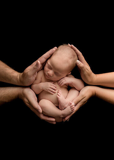 Parent hands are holding a new baby on a black background.