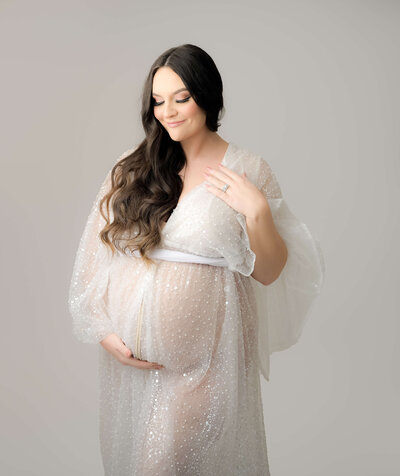 Alexa  poses for her Bremerton studio high key maternity photo session in a stunning sheer white sequin robe..