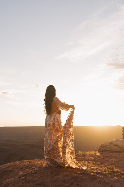 photo of bride while she's standing on a rock cliff holding up her wedding gown taken by a Elopement photographer near me