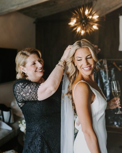 Bride smiling as her mother adjusts her veil after makeup and hair prep in Bethel, CT.