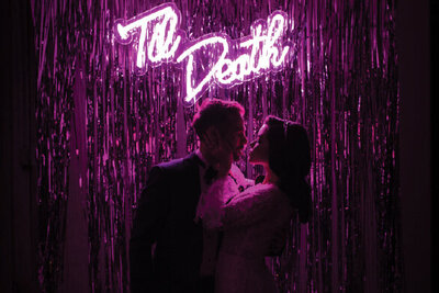 Bride and groom kissing in front of neon sign
