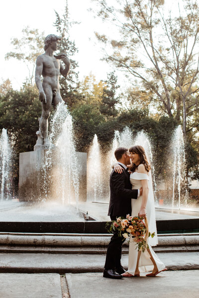 bride and groom hugging in front of a water fountain