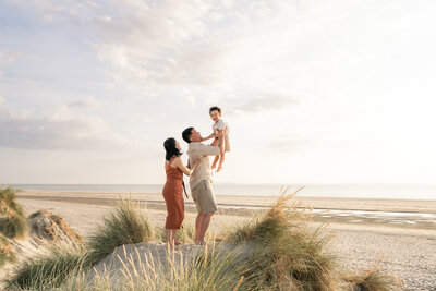 Parents on Sussex West Witterings Beach, lifting boy into the air whilst standing on the dunes.