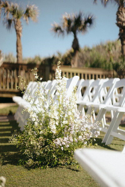 Wildflower-inspired floral aisle arrangement at an outdoor wedding, a ceremony design curated by The Eventful Gals.