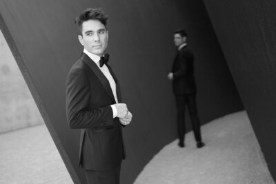 Groom in tuxedo poses confidently with modern architectural backdrop