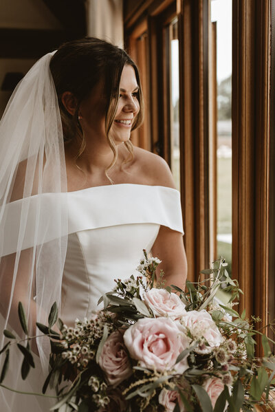 Pink and white with green foliage bridal bouquet flowers in natural light with bride smiling in a white dress