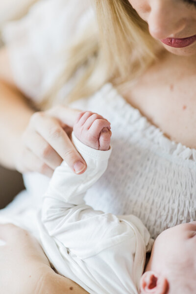 Newborn wraps hand around blonde mother's finger  at their Little Rock home