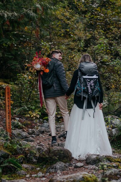 couple holds hands in forest with backpacks