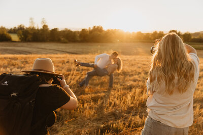 two photographers shooting a couple in a grassy field at golden hour