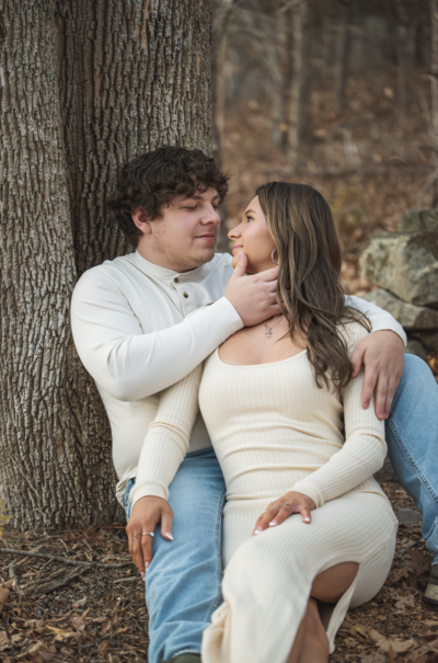 Intimate portrait of young couple, sitting against a tree in the woods.
