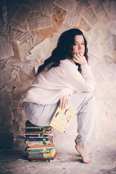 A woman sitting on top of a stack of books, captured beautifully by Shreveport portrait photographer Britt Elizabeth