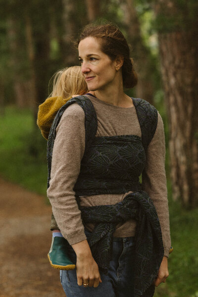 Foto einer Frau, die ihr Kind in einem Tragetuch trägt im Wald