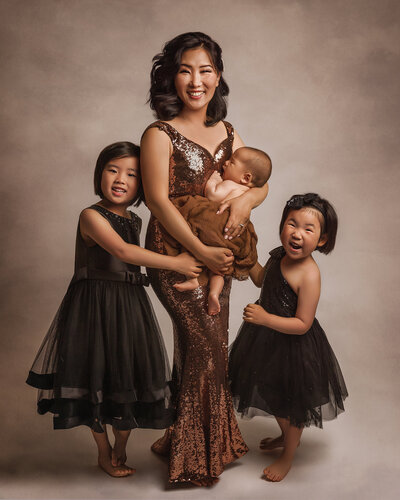 mother of 3 wearing a gold sequin gown and two girls in black dresses on brown background near dupont