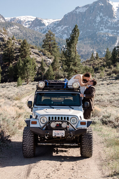 A bride seated atop a jeep leans over to kiss her groom while on their wedding day in Mammoth Lakes