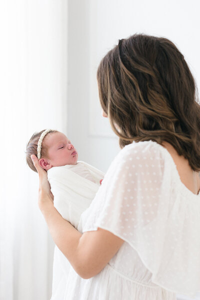 Mom snuggling her swaddled newborn in a bright northern kentucky newborn photography studio