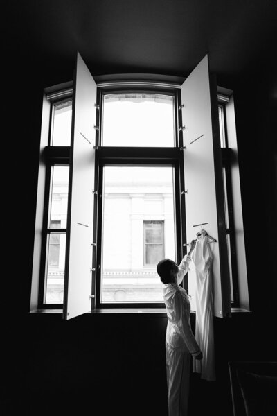 Une mariée prend sa robe qui est accrochée dans la fenêtre de sa chambre d'hôtel.