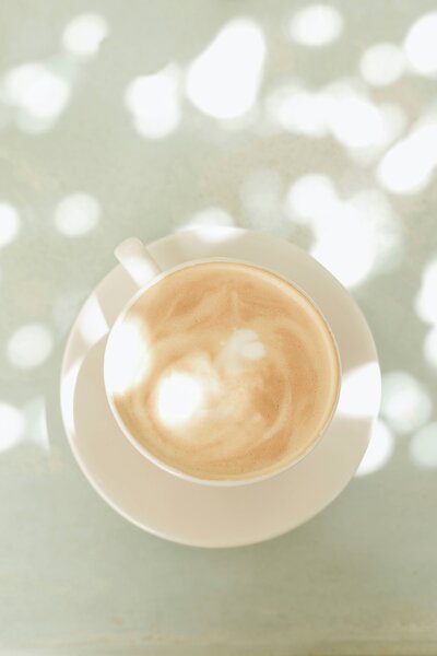 Flatlay of a warm latte in a white cup with sunlight streaming in, reflecting the photographer’s love of cozy, slow mornings.