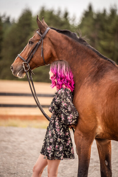 high school senior equestrian rests her head against large hunter/jumper gelding