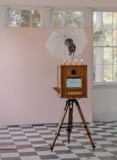 Vintage wooden photo booth on tripod with checkered flooring and pink backdrop, set up before event guests arrive.