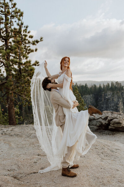 groom lifting bride, bride holding veil and looking off into the distance