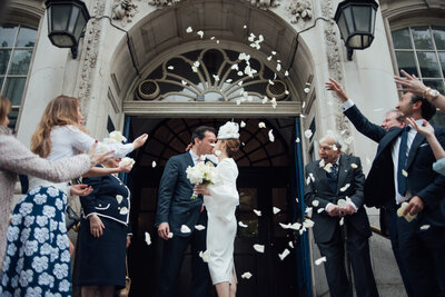 A newly married couple sharing a kiss whilst wedding guests throw confetti over them taken by London Wedding Photographer Liberty Pearl