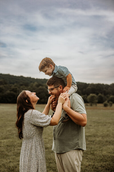 Indianapolis Family sitting in a field, holding baby up as they smile at the camera
