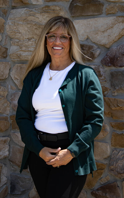 Steph Traver posing for a headshot behind a rustic stone wall. 